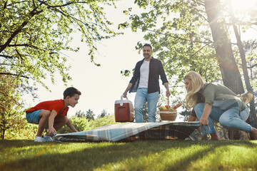 Happy young mother and father with little boy smiling while having picnic outdoors