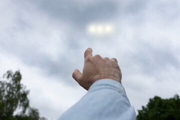 Man pointing finger at the strange lights in the sky, three light orbs among the clouds, UFO concept