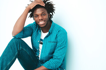 Portrait of handsome smiling hipster lambersexual model.Unshaven African man dressed in summer stylish clothes. Fashion male with dreadlocks hairstyle posing near light blue wall in studio