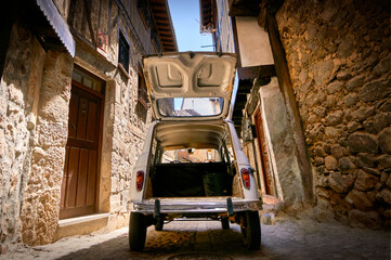 Fototapeta na wymiar Wide Angle Rear View White Historic Vehicle With Open Trunk On Narrow Cobblestone Street In A Village