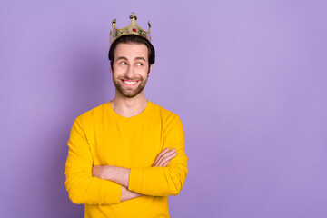 Portrait of attractive cheerful man wearing crown looking aside copy space isolated over pastel...