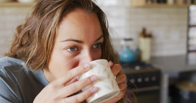 Thoughtful caucasian woman in sunny cottage kitchen drinking coffee