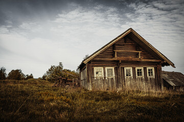 Obraz premium An old, abandoned log house. Deserted village in Russia. A lonely hut without people. Rotten wall construction. Hut against the background of the blue sky. Karelia. Russia. Day.