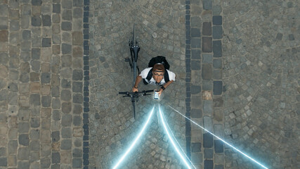 Young stylish guy walks with bicycle around the city using mobile smartphone. Online communication. 5G internet connecting. Freelance lifestyle. Top view of modern pavement road for bike transport.