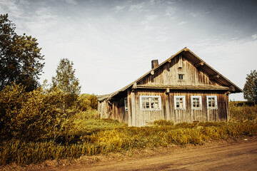 Fototapeta premium An old, abandoned log house. Deserted village in Russia. A lonely hut without people. Rotten wall construction. Hut against the background of the blue sky. Karelia. Russia. Day.