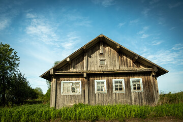 An old, abandoned log house. Deserted village in Russia. A lonely hut without people. Rotten wall construction. Hut against the background of the blue sky. Karelia. Russia. Day.