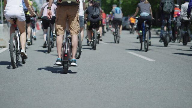 Slow motion partial view of man riding mono wheel on asphalt road in crowd of cyclists. Following shot contestants of street race. Outdoor activity. Concept of healthy lifestyle