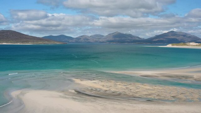 4k short clip of waves at Seilebost and Luskentyre beaches, Isle of Harris. Taken from high viewpoint on sunny day, blue sky and clouds. White sand, turquoise sea, mountains.