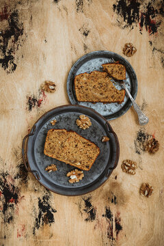 A vertical top view image of a carrot apple walnut loaf cake. Slices of cake on vintage metal plates, wooden backdrop.