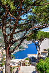 Positano, Italy. May 27th, 2020. Picturesque generic view from a small street in positano with maritime pine trees in the foreground, the houses on the hills and the sea in the background.