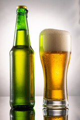 pouring beer into beer glass and foam and green transparent bottle with beer beside