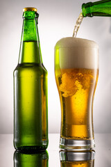 pouring beer into beer glass and foam and green transparent bottle with beer beside