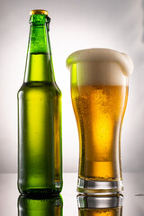 pouring beer into beer glass and foam and green transparent bottle with beer beside