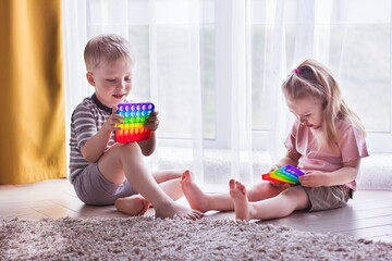 Blonde boy and girl Kids play with pop it sensory toy. Trendy silicon fidgeting game for stressed...