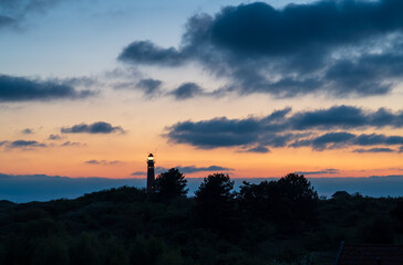 Lighthouse in the dunes and clouds during sunset.