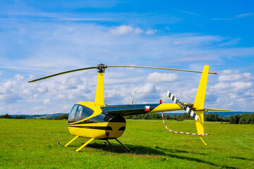 Fototapeta na wymiar Modern small light helicopter on a grassy field against the blue sky.