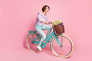 Full size profile side photo of young attractive happy excited crazy girl riding bicycle fast isolated on pink color background