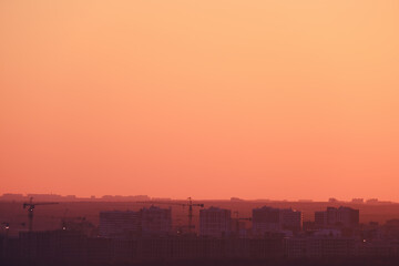 Fototapeta premium Buildings in a city under construction against the background of an orange sunset sky, copy space