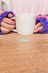 Woman's hands with white cup and letter blocks on wooden table. Coffee text and a heart