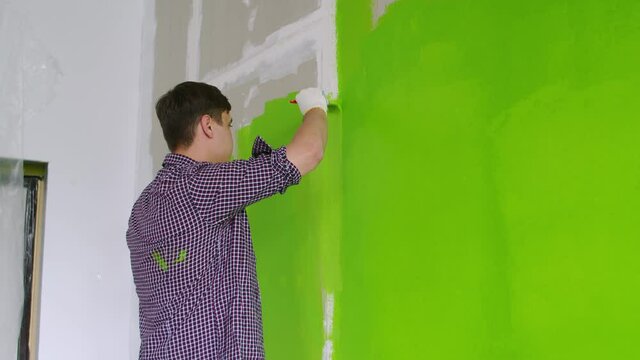 The guy paints the wall with a brush in green, the view from the back