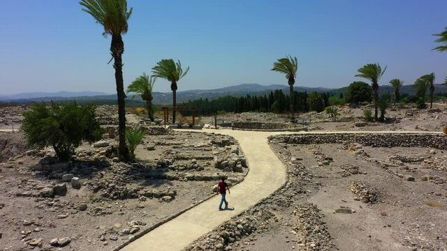 Aerial Shot Of Man Walking On Footpath At Tel Megiddo Against Sky, Drone Ascending Over Tourist Exploring Protected Site On Sunny Day