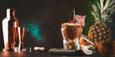 Pina Colada Summer Cocktail in chopped coconut with tropical fruits and copper bar tools, copy space