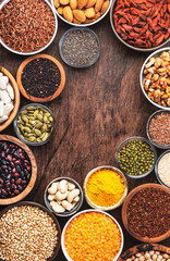 Superfoods, legumes, cereals, nuts, seeds set in bowls on wooden background. Superfood as chia, spirulina, beans, goji berries, quinoa, turmeric and other. Top view