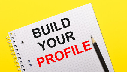 Obraz premium White notebook with inscription BUILD YOUR PROFILE written in black pencil on a bright yellow background.
