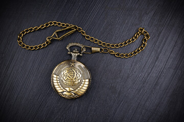 Bronze closed pocket watch with Soviet Union coat of arms and chain on dark surface.