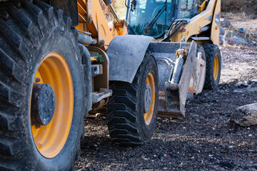 The large yellow wheels of a tractor with black tire, covered in mud, hydraulic foot and bucket. Digging machinery parts, industry detail of bulldozer shovel. Construction excavator dirty bucket teeth