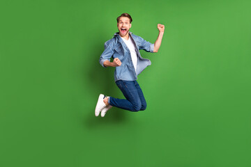 Fototapeta na wymiar Full length body size photo of young guy jumping high gesturing like winner isolated bright green color background