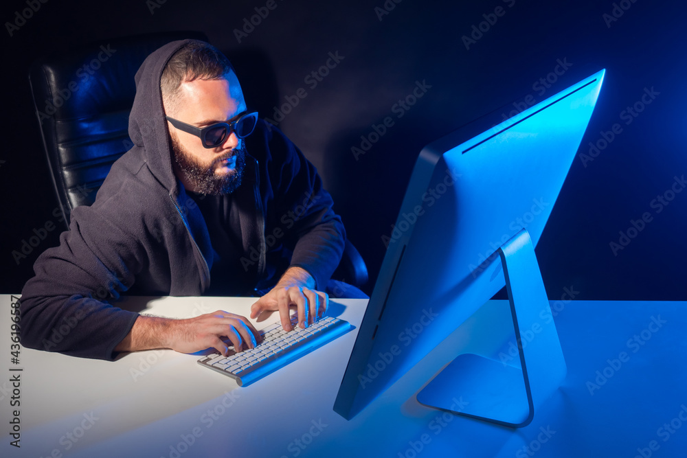 Poster a man in a black hoodie and glasses is working at a computer. programmer at work. a man writes a com