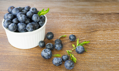 Ripe blueberries in a white porcelain cup on a wooden background
