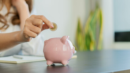 A young woman who puts coins in a piggy bank with accounting, planning and money saving ideas.