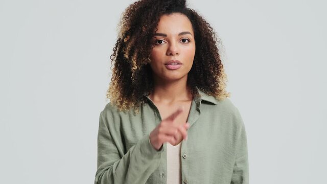 A positive african american woman with afro curls is doing silence gesture standing isolated over a white wall in the studio