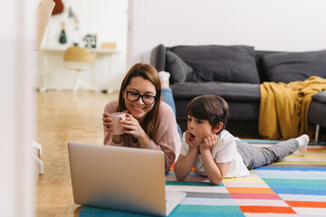 mother and child laying on the floor and using laptop computer