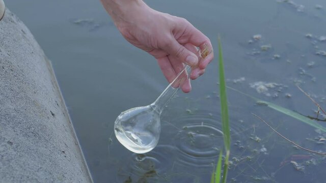 Close-up of a man drawing water into a glass flask from a polluted lake