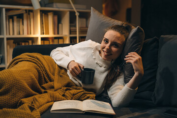 Fototapeta premium woman reading book at home. she is relaxing on a sofa at home