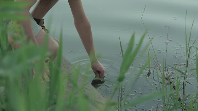 Close-up of a man drawing water into a glass flask from a polluted lake