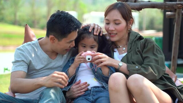 Happy asian young family tourists sitting on couch taking photo together on green grass at  countryside in nature park in morning outdoors on vacation or holiday . father mother and daughter .