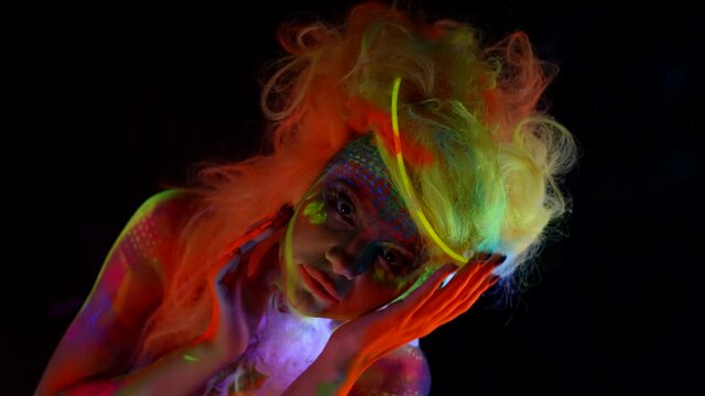 sexy lady with creative fluorescent makeup and body art, glowing in darkness with UV lights