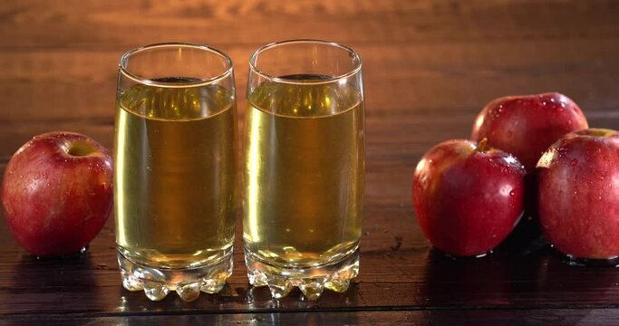 Man pust fresh healthy apple juice glass on wooden table. Two glasses with juice on the surface. Tasty juice in summer day. Apples on the table too