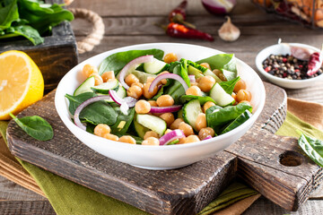 Chickpea salad with cucumber, spinach, parsley, onions and lemon in a plate on a served table. Tasty and healthy vegetarian food, oriental and Mediterranean cuisine.