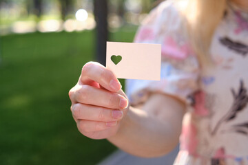 White card with a cut out heart in the hands of a girl in the rays of the sun. Close-up postcard. Form for congratulations. Romantic invitation. Mockup. Empty space for a message or invitation