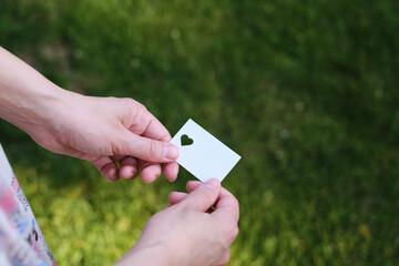 White card with a cut out heart in the hands of a girl in the rays of the sun. Close-up postcard. Form for congratulations. Romantic invitation. Mockup. Empty space for a message or invitation