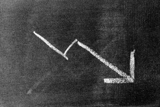 White chalk hand drawing in arrow down shape on blackboard or chalkboard background (Concept of stock decline, down trend of business, economy)