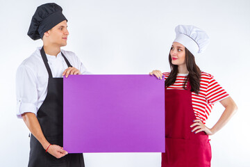 Two chefs cooks show a blank poster. Pink poster in hands of chefs. Young man and woman are working cooks. Concept - students of cook advertise something. Restaurant staff. They work in restaurant.