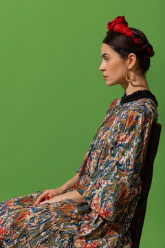 Portrait of young beautiful woman in image of famous painter, artist Frida Kahlo on green background. Side view