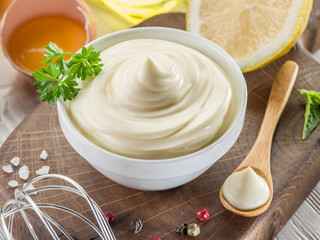 Bowl with mayonnaise sauce in the centre and mayonnaise ingredients around it on wooden table....