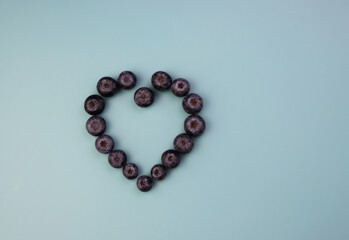 Blueberries are laid out in the shape of a heart. Fresh blueberries on a blue background. 
